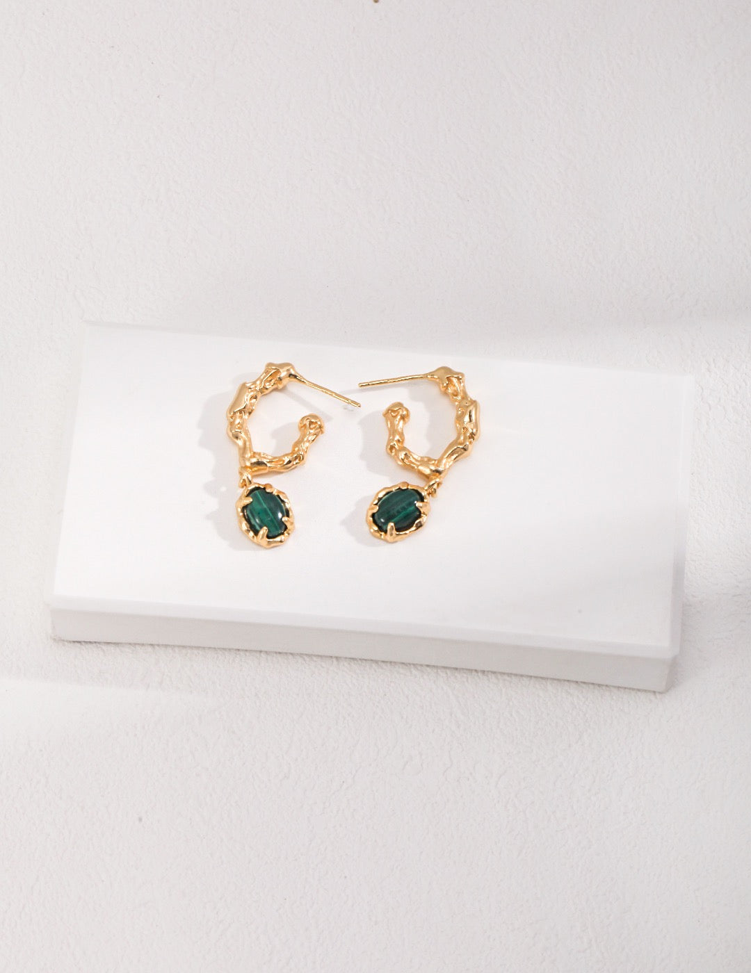 Emerald earrings with gold setting on a white background, elegant and timeless design.
